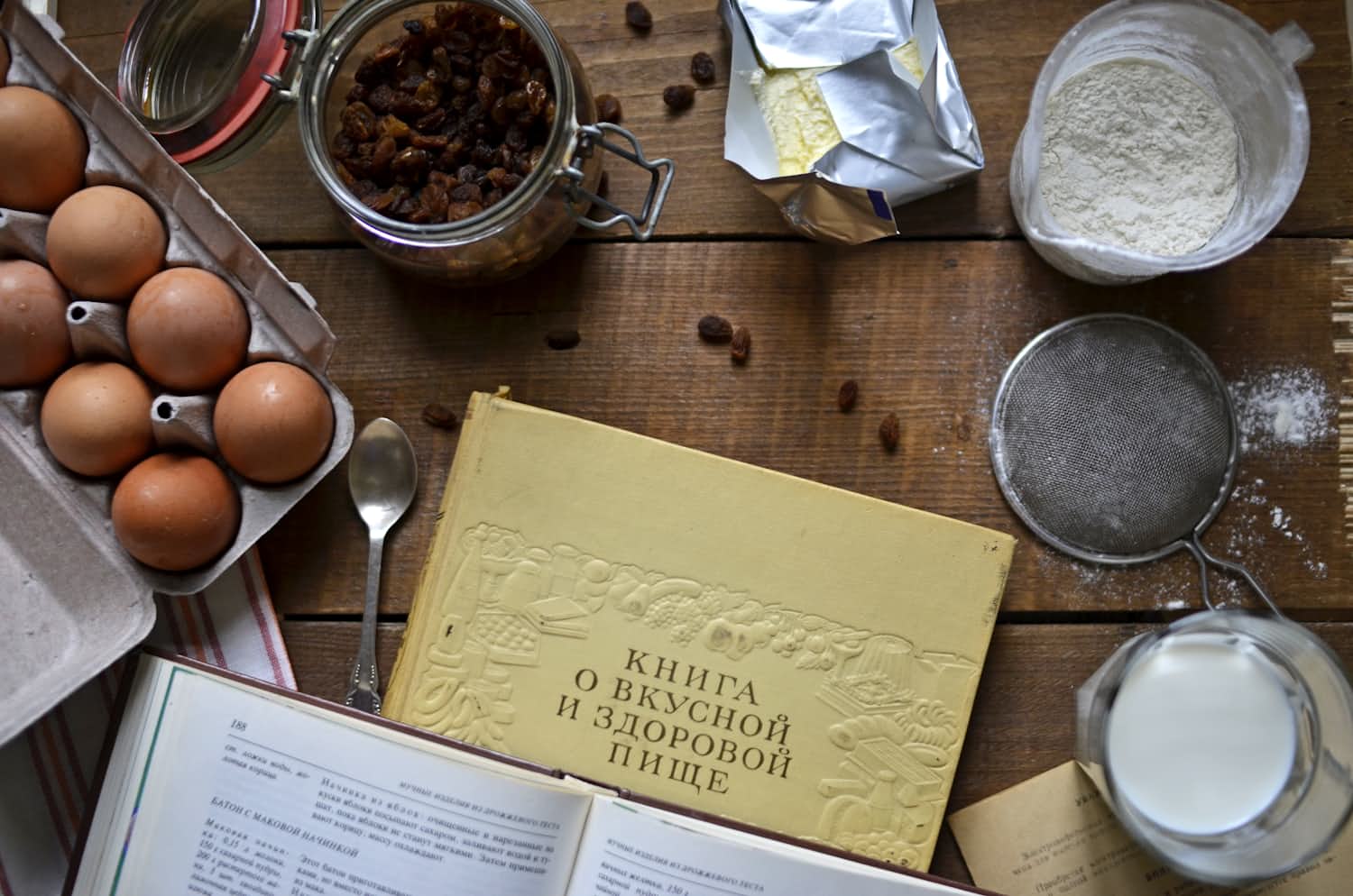 Overhead view of an open cookbook and kitchen notes on a wooden table